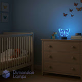The Monarch Butterfly LED 3D lamp used as a night light in a child's bedroom, casting a soothing blue glow amongst butterfly wall decorations. Nursery gift idea.