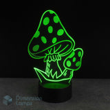 A 3D optical illusion night light shaped like mushrooms, glowing bright green against a black background. The lamp has a black cylindrical base and is shown on a dark grey surface. Fantasy gift idea. 