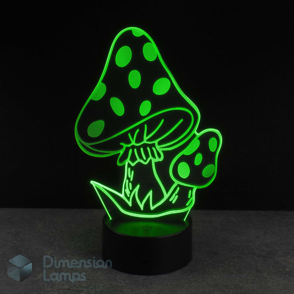 A 3D optical illusion night light shaped like mushrooms, glowing bright green against a black background. The lamp has a black cylindrical base and is shown on a dark grey surface. Fantasy gift idea. 