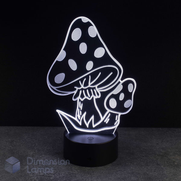 A 3D optical illusion night light shaped like two spotted mushrooms, glowing with white light on a black base against a dark background. A 'Dimension Lamps' watermark is visible in the bottom-left corner.