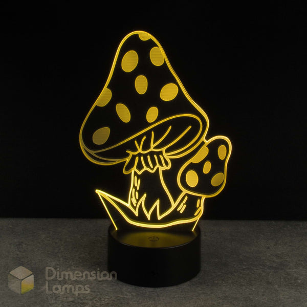 A mushroom-shaped 3D LED night light glowing with warm yellow light, featuring a large spotted mushroom and smaller mushroom on a black cylindrical base, set against a dark background.