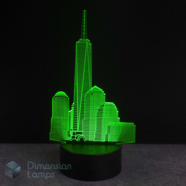 A 3D optical illusion LED lamp depicting the New York City skyline, illuminated in bright green on a black cylindrical base against a dark background.