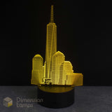 A 3D optical illusion lamp depicting the One World Trade Centre skyline, illuminated in a bright yellow colour, set against a dark black background.