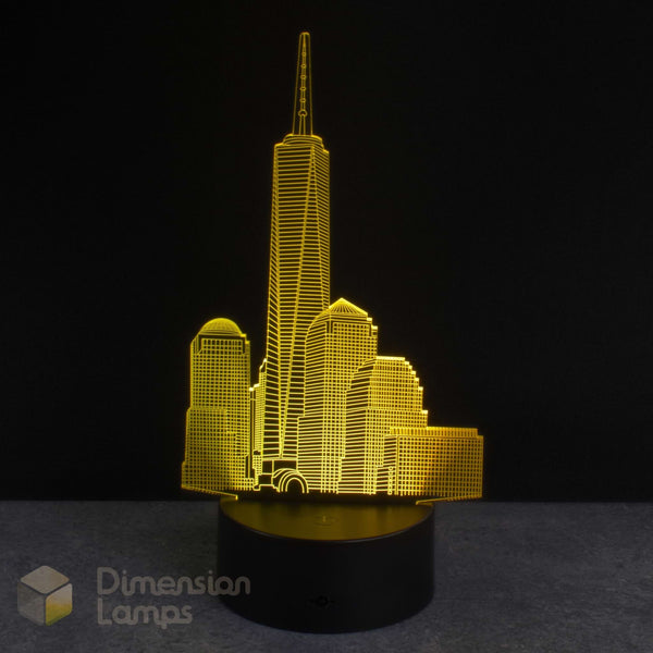 A 3D optical illusion lamp depicting the One World Trade Centre skyline, illuminated in a bright yellow colour, set against a dark black background.