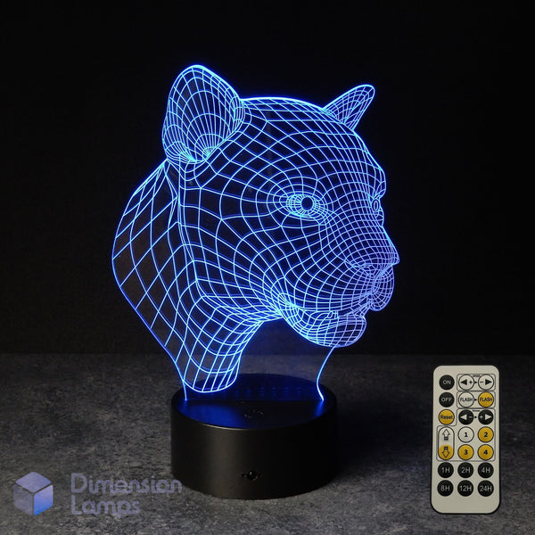 A 3D optical illusion LED night light shaped like a panther or big cat head, glowing with blue light on a black base, shown with a white remote control against a dark background. The Aussie brand name 'Dimension Lamps' is visible as a watermark in the bottom-left corner. Gift idea for Panther lovers.