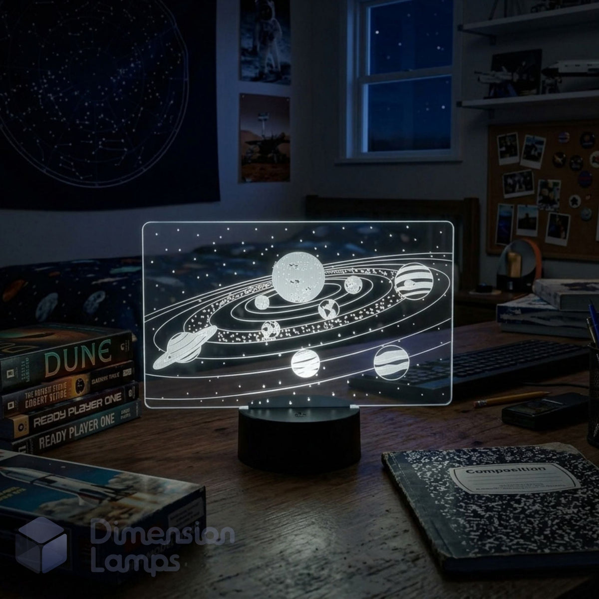 A glowing holographic solar system lamp on a wooden desk in a dimly lit bedroom. The translucent panel shows white and grey planets and rings.