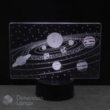 An LED night light with a clear acrylic panel displaying a white solar system design, mounted on a black cylindrical base against a dark background.