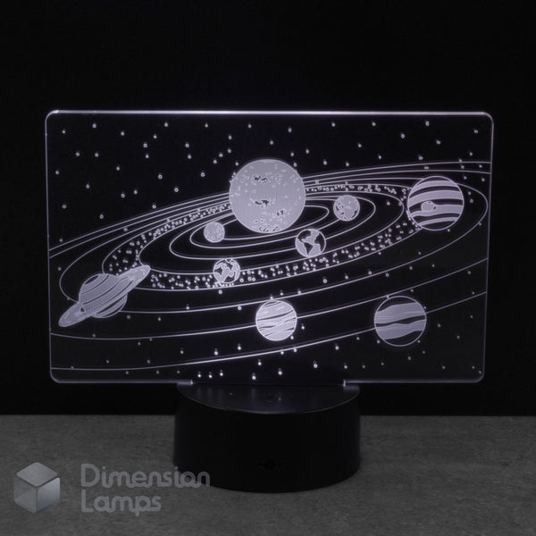 An LED night light with a clear acrylic panel displaying a white solar system design, mounted on a black cylindrical base against a dark background.
