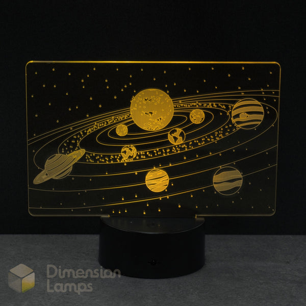 A Dimension Lamps solar system night light featuring a glowing gold acrylic panel with etched planets, stars, and orbital paths on a black base.