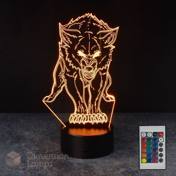 A 3D optical illusion night light shaped like a snarling wolf, glowing with warm orange light from a black base, shown on a dark surface with a small remote control in the lower right corner.