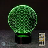 A 3D optical illusion LED lamp shaped like a golf ball, glowing with a bright green pattern on a black base, shown with a 7 colour sleep timer remote control against a dark background.
