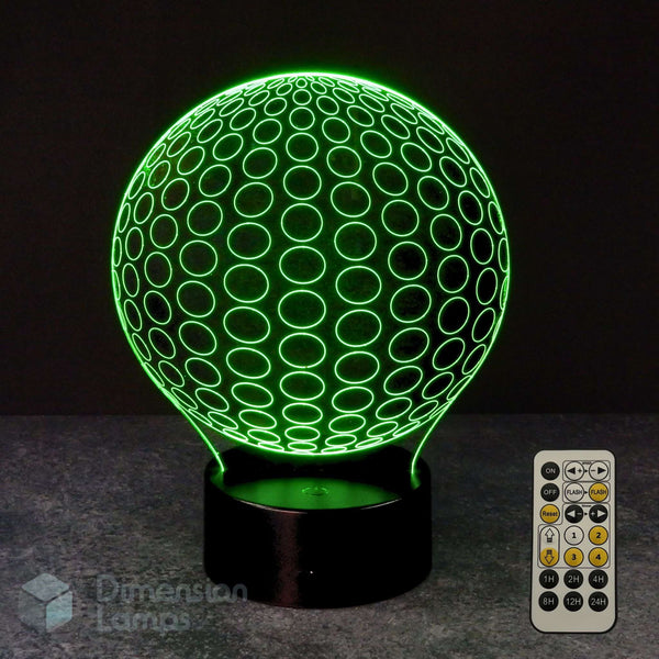 A 3D optical illusion LED lamp shaped like a golf ball, glowing with a bright green pattern on a black base, shown with a 7 colour sleep timer remote control against a dark background.