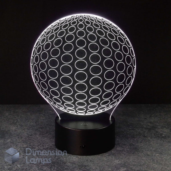 A 3D optical illusion lamp shaped like a glowing white sphere with circular patterns, resting on a black cylindrical base against a dark background.
