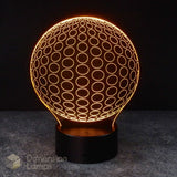 A 3D optical illusion LED lamp by Dimension Lamps, featuring a glowing orange sphere with a circular pattern and a black cylindrical base, set against a dark background. Teen study aid lamp.
