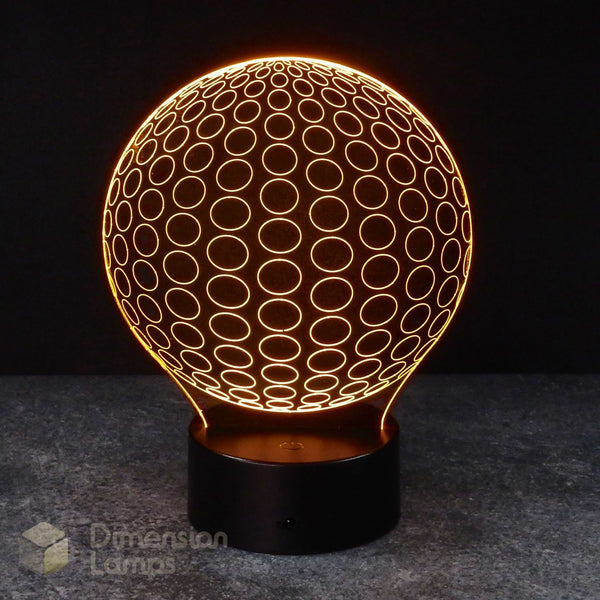 A 3D optical illusion LED lamp by Dimension Lamps, featuring a glowing orange sphere with a circular pattern and a black cylindrical base, set against a dark background. Teen study aid lamp.