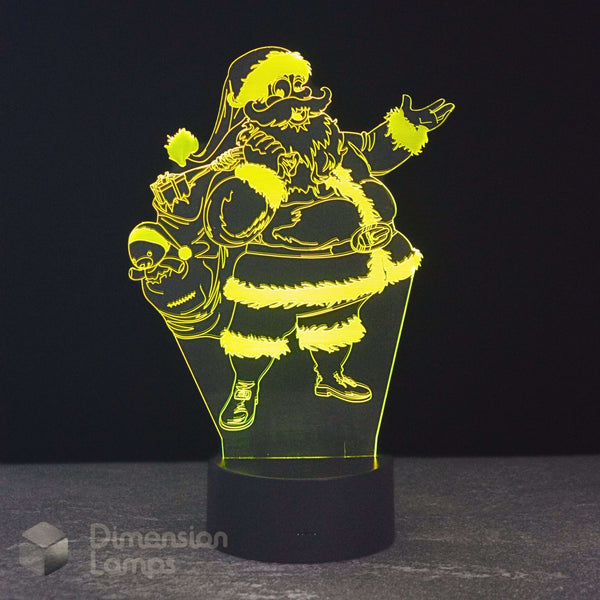 A 3D optical illusion LED night light depicting Santa Claus carrying a sack of gifts, glowing with a bright yellow light on a black base against a dark background.