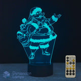 A 3D optical illusion LED night light shaped like Santa Claus carrying a sack, glowing with a bright cyan-blue light. The lamp is shown on a dark surface against a black background, with a white remote control in the bottom right corner and a 'Dimension Lamps' logo watermark in the bottom left.