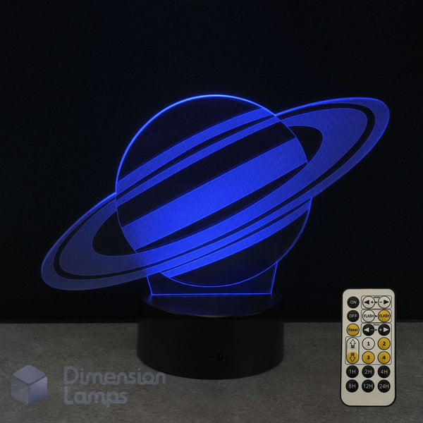 A Saturn 3D optical illusion lamp glowing with blue light, 7-colour remote control on a dark surface against a black background. Kids space lamp.