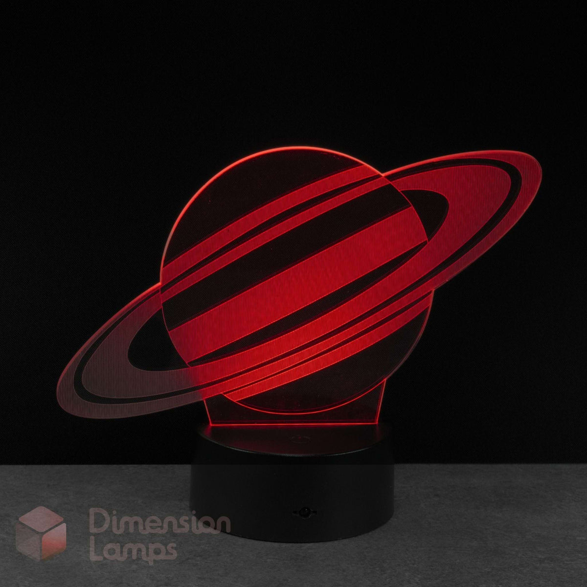 A red Saturn 3D optical illusion lamp with a black base against a dark background. A 'Dimension Lamps' watermark is visible in the bottom corner.