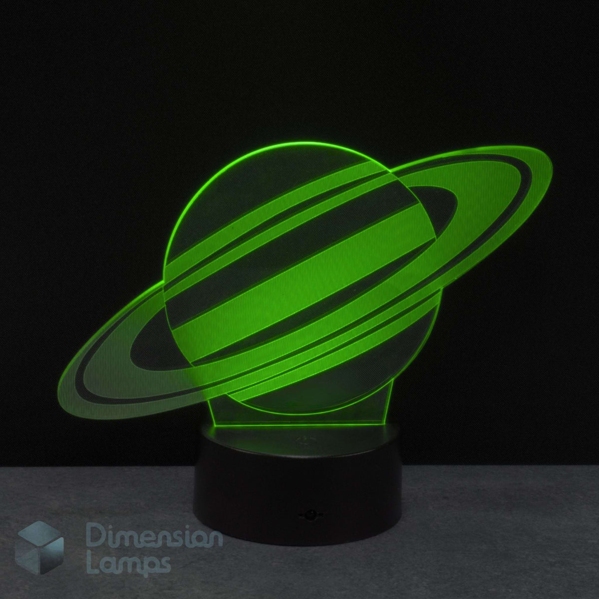 A 3D illusion LED night lamp of the planet Saturn, glowing bright green on a black base against a dark background. Gift for kids interested in space.