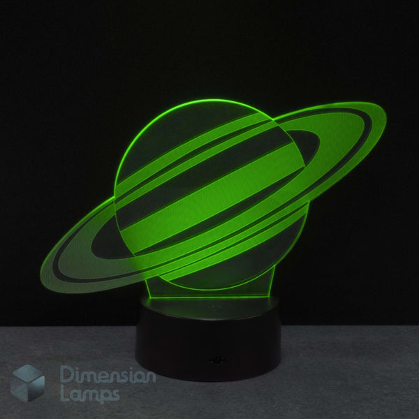 A 3D illusion LED night lamp of the planet Saturn, glowing bright green on a black base against a dark background. Gift for kids interested in space.