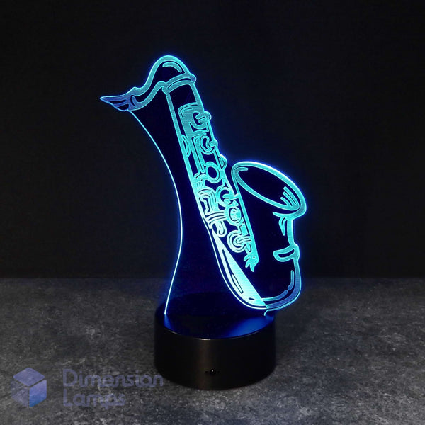 A 3D optical illusion LED lamp shaped like a saxophone, glowing with a bright blue light on a black base against a dark background. Saxophonist gift idea.