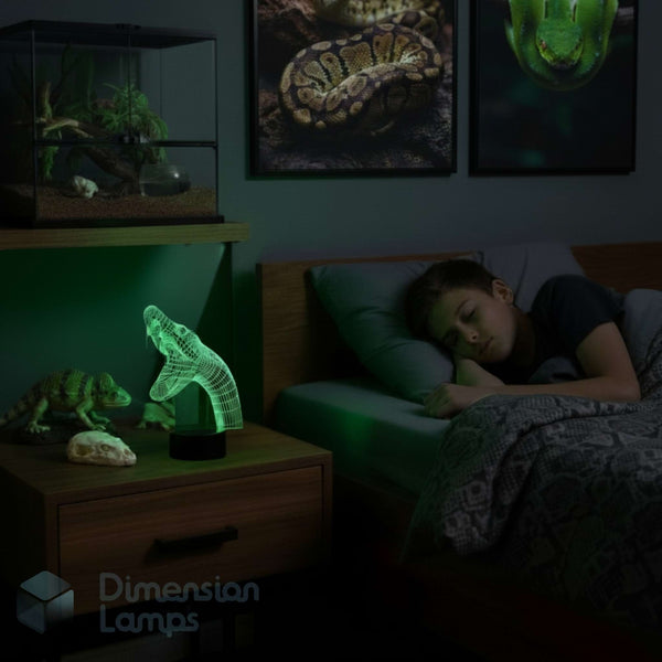 A teenager sleeping in bed in a dark bedroom, with a glowing green 3D-effect lamp shaped like a snake on a bedside table. The room is dimly lit, and framed snake artwork hangs on the wall.