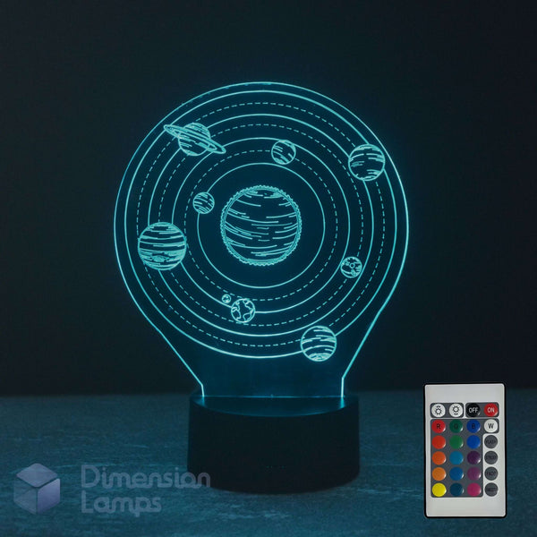 A 3D optical illusion night light shaped like a light bulb, displaying a glowing solar system design with planets and rings. The lamp is on a dark surface with a dark background, with a 16 colour remote control in the bottom right corner and a 'Dimension Lamps' watermark in the bottom left.