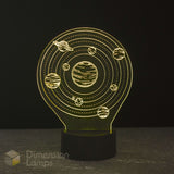 A 3D optical illusion night light shaped like a solar system, featuring a glowing design with planets and rings on a black base. The lamp is photographed against a dark background.