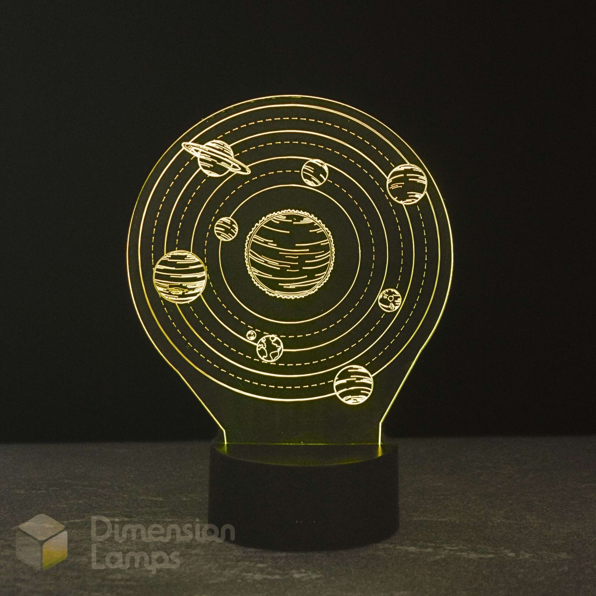 A 3D optical illusion night light shaped like a solar system, featuring a glowing design with planets and rings on a black base. The lamp is photographed against a dark background.