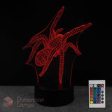 A red LED spider-shaped 3D optical illusion night light on a black base, shown with a 16 colour remote control against a black background. The brand name 'Dimension Lamps' is visible as a watermark in the bottom-left corner.