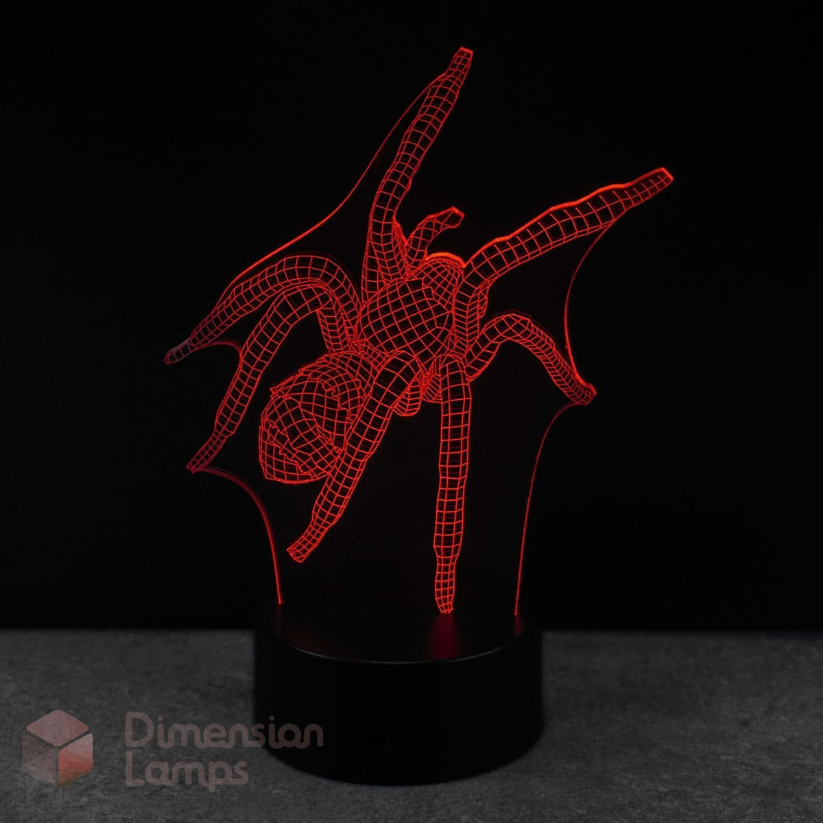 A red LED 3d illusion lamp of a spider, mounted on a black cylindrical base against a dark background. A 'Dimension Lamps' watermark is visible in the bottom-left corner. Arachnid gift idea for teens.