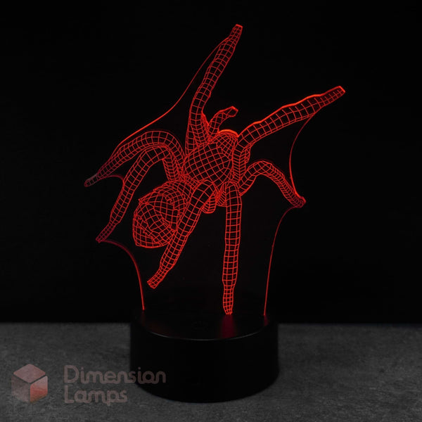 A red LED 3d illusion lamp of a spider, mounted on a black cylindrical base against a dark background. A 'Dimension Lamps' watermark is visible in the bottom-left corner. Arachnid gift idea for teens.