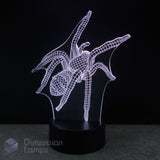 A 3D optical illusion LED night light shaped like a spider, glowing with a white wireframe design on a black base against a dark background. A 'Dimension Lamps' watermark is visible in the bottom-left corner. Spider gift for teens. 