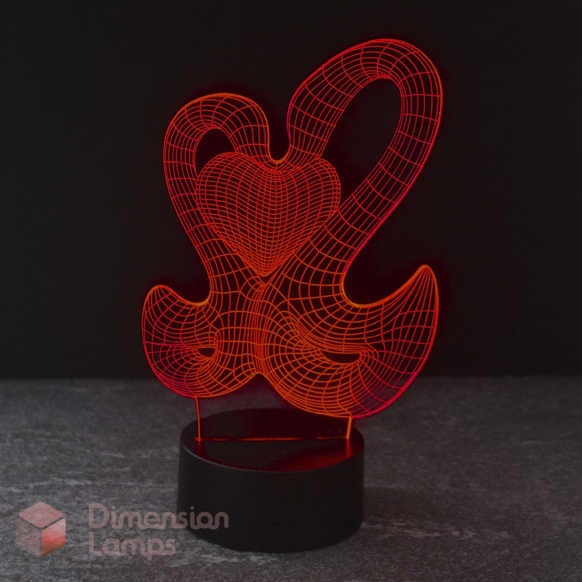 A 3D optical illusion LED night light featuring a 2 interlocking swans forming a red heart on a black cylindrical base, set against a dark background.