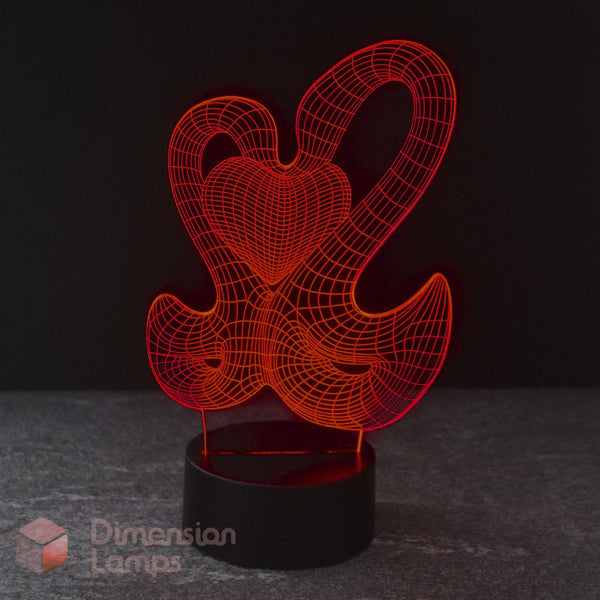A 3D optical illusion LED night light featuring a 2 interlocking swans forming a red heart on a black cylindrical base, set against a dark background.