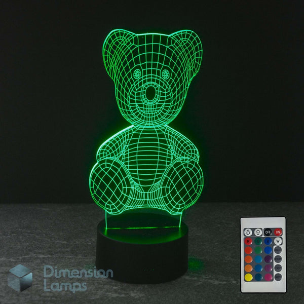 A 3D optical illusion LED night light of a teddy bear, glowing with green on a black base with a 16 colour remote control and a Dimension Lamps logo.