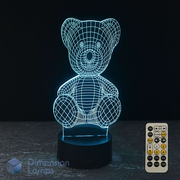 A 3D LED light of a teddy bear, glowing cyan wireframe on a black base, with a 7 colour remote control on a dark background and a Dimension Lamps logo