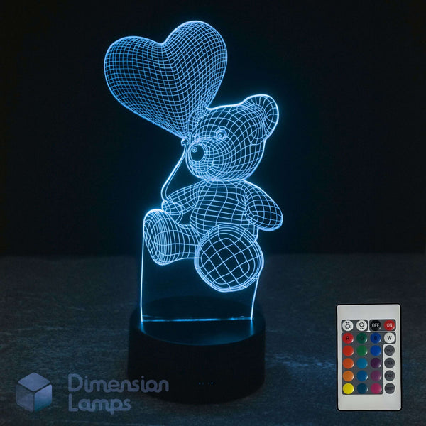 3D optical illusion LED lamp of a teddy bear holding a heart balloon, glowing blue on a dark base. 16 colour remote control and Dimension Lamps logo.