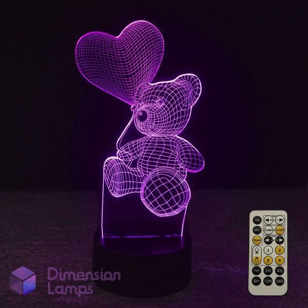 A 3D optical illusion LED night light lamp of a teddy bear holding a heart, glowing purple with a 7 colour remote control and 'Dimension Lamps' logo.