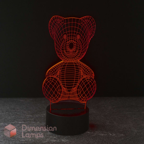 A 3D optical illusion LED night light of a teddy bear, glowing red on a black base against a dark background. Dimension Lamps logo in the bottom-left.