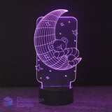 A 3D LED night light featuring a teddy bear sleeping on a crescent moon with stars, glowing purple on a black base. Calming night light for kids. 