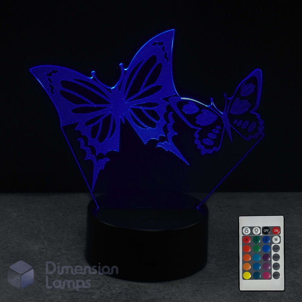 A 3D optical illusion LED night light with two butterflies on a black base, shown with a 16 colour remote control against a dark background. 