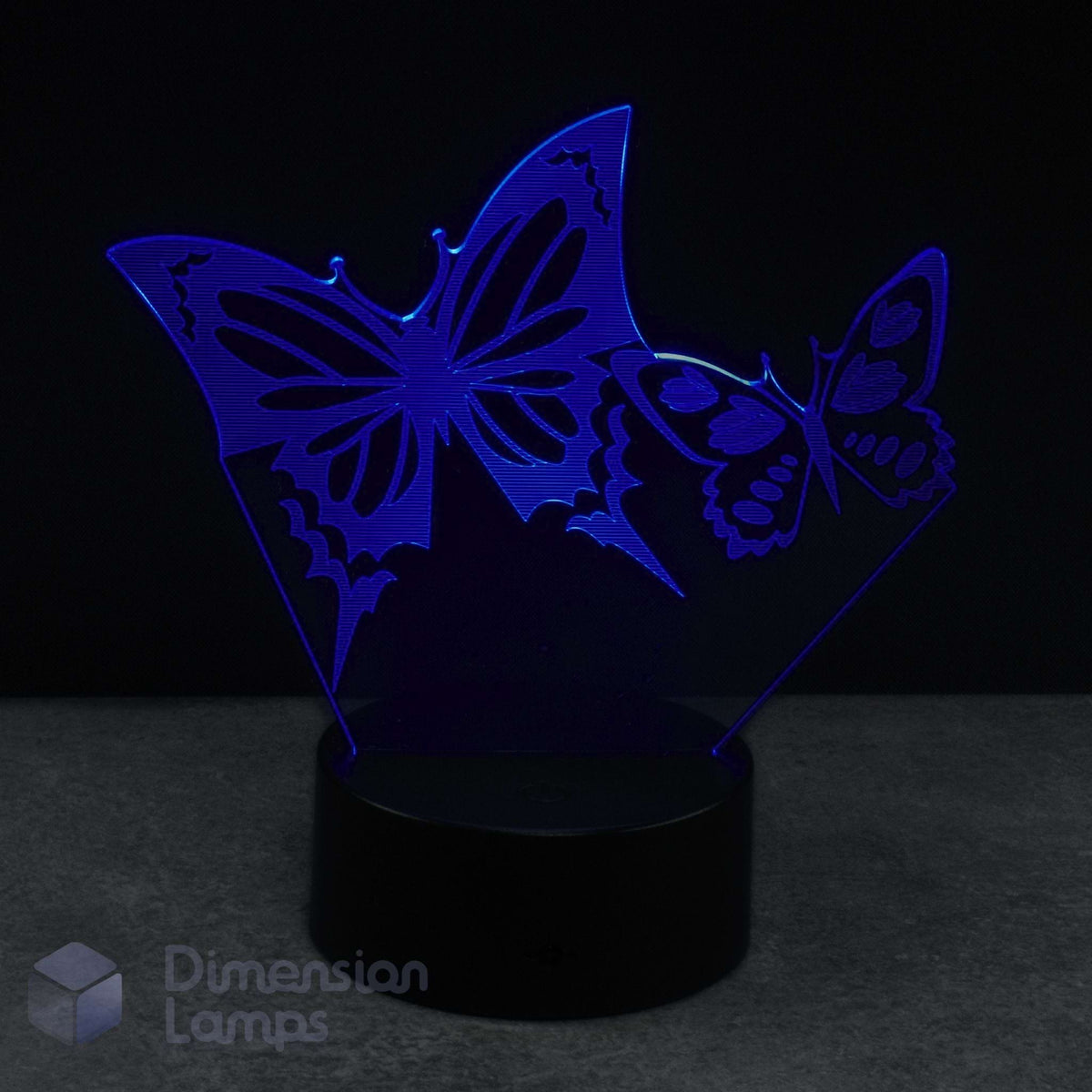 A 3D acrylic illusion lamp featuring two glowing blue butterflies on a black base against a dark background with a 'Dimension Lamps' logo.