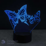 A 3D optical illusion LED night light featuring two glowing cyan butterfly silhouettes on a black base, against a dark background. Girls gift idea.
