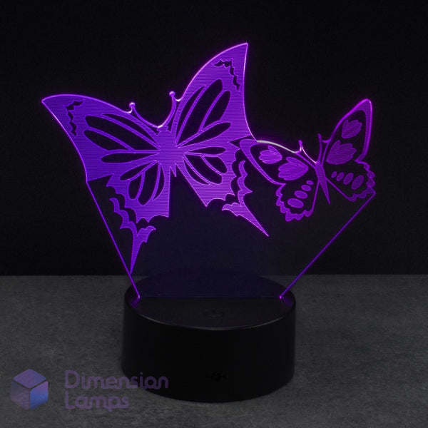 A 3D laser-cut butterfly-shaped LED night light on a black cylindrical base, glowing with a purple light against a dark background. 