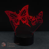 A 3D laser-cut acrylic night light featuring two glowing red butterflies on a black base against a dark background. 