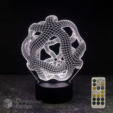 A 3D optical illusion lamp with a white wireframe warped space design on a black base, shown alongside its 7 colour sleep timer remote control against a dark background.