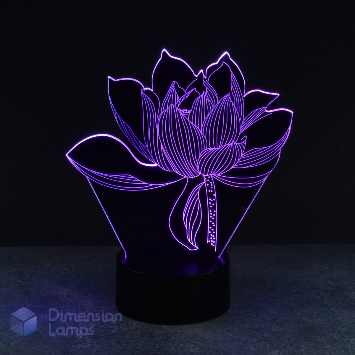 A purple illuminated 3D lamp in the shape of a lotus flower sits on a black circular base against a dark background. This floral-inspired design acts as a unique bedside light and a peaceful home accent.