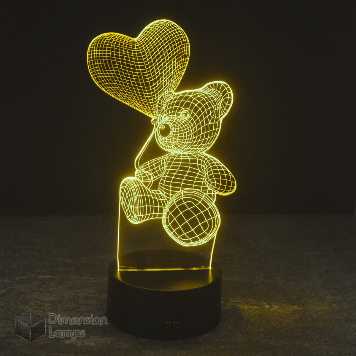 A yellow-toned 3D illusion lamp in the form of a teddy bear clutching a heart-shaped balloon. This night light provides a soft, ambient glow, ideal for children's bedrooms and adding a touch of whimsy to décor. 